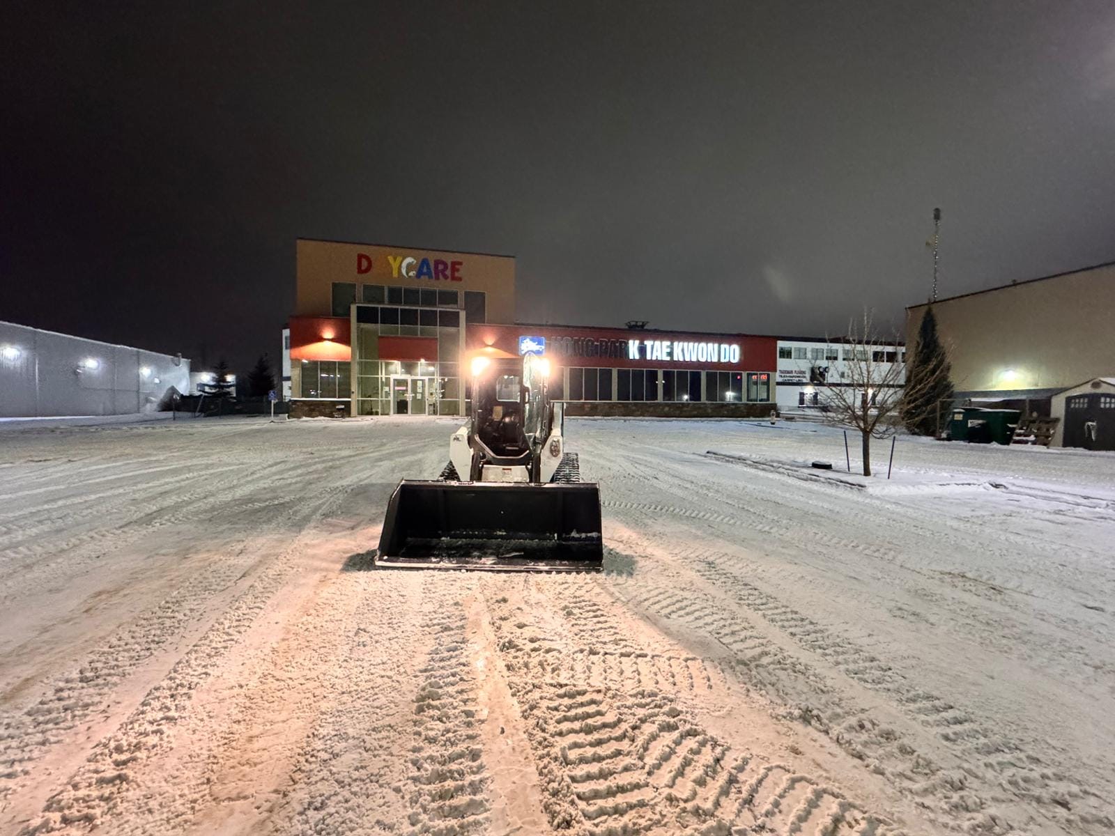 Skid steer clearing a commercial lot at night in Edmonton