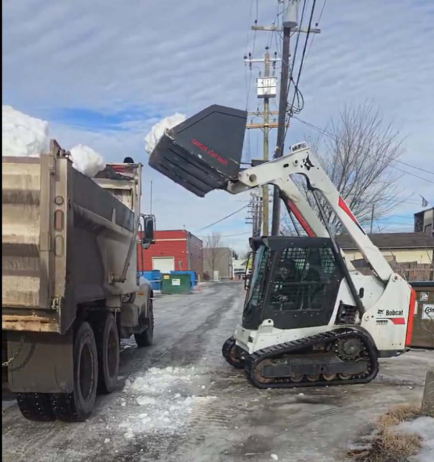 Skid steer loading snow into a dump truck for off-site hauling in Edmonton