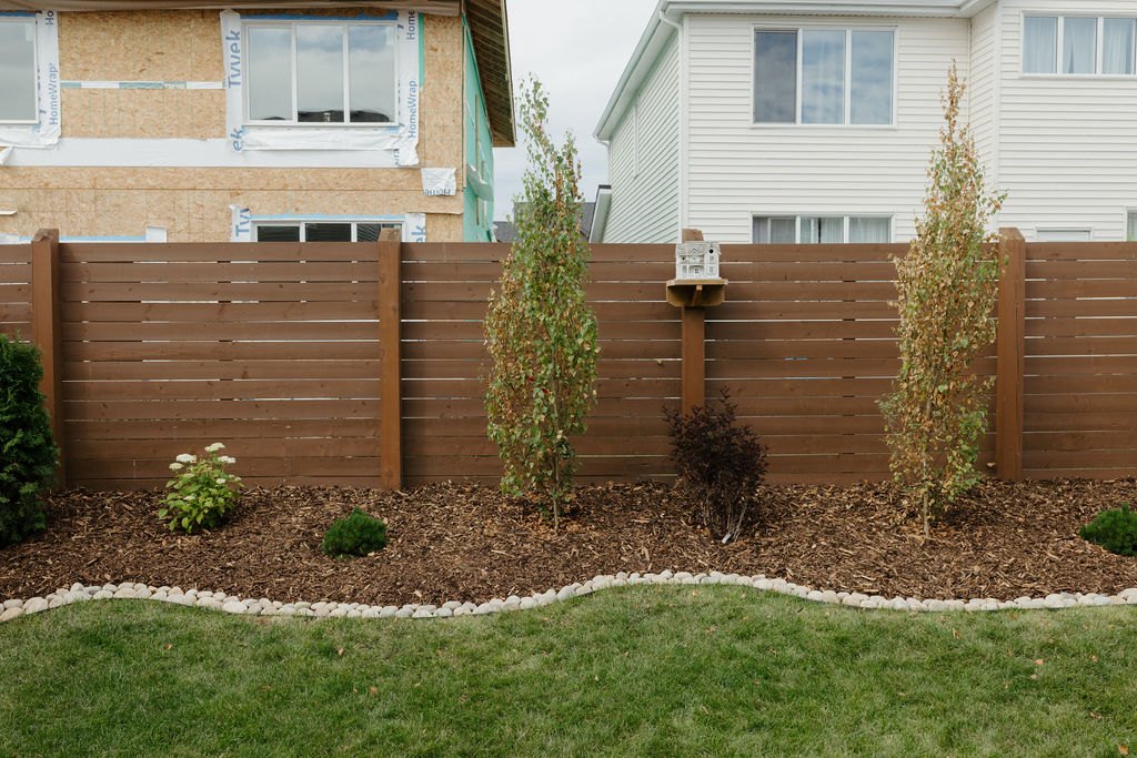 New horizontal cedar fence with a fresh planting bed and lawn